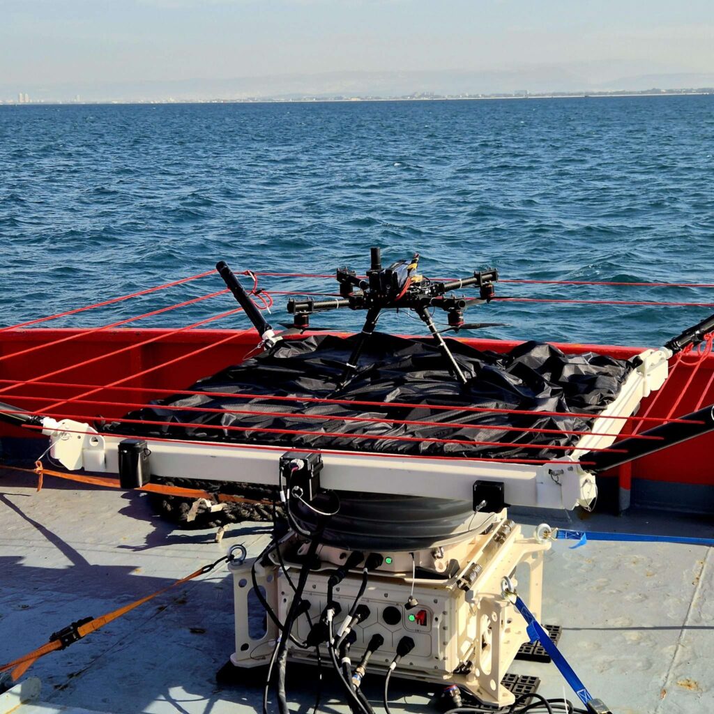Laboratory equipment with numerous cables mounted on a platform by the ocean, distant coastline on the horizon.