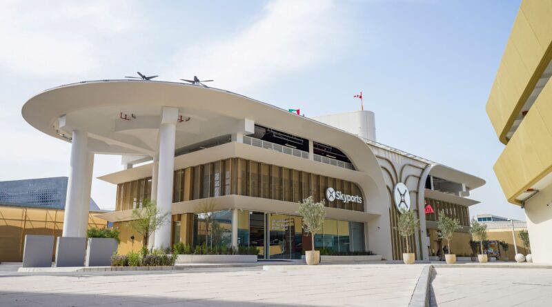 Exterior view of a modern Skyports building with a curved white canopy, tall pillars, and a paved plaza.