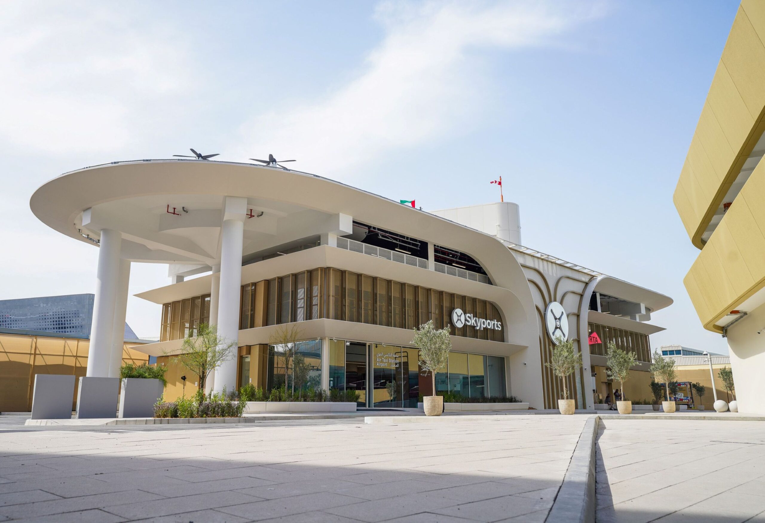 Exterior view of a modern Skyports building with a curved white canopy, tall pillars, and a paved plaza.