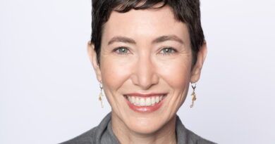 Smiling woman with short dark hair, visible green eyes, wearing a gray turtleneck sweater.