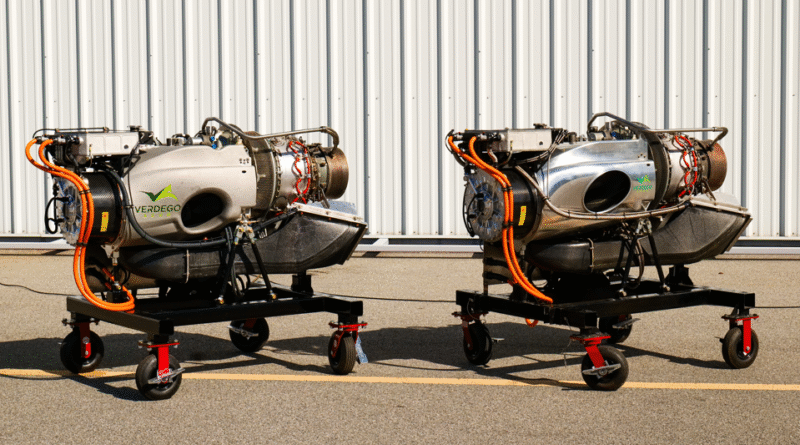 Two small jet engines on mobile stands side by side in a hangar, with orange hoses and a corrugated metal wall behind them (VERDEGO branding).