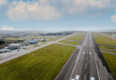 Cornwall Airport Newquay - eVTOL Insights Aerial view of a rural airport showing a long runway with multiple taxiways, hangars, and surrounding green fields under a blue sky.