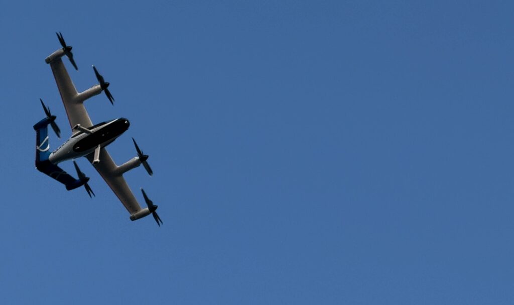 Large propeller aircraft in flight against a clear blue sky, viewed from the side below the wings orientation downward left.