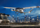 Sleek silver futuristic airplane landing over a brightly lit city skyline at dusk/night.