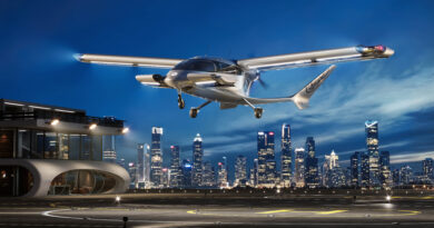 Sleek silver futuristic airplane landing over a brightly lit city skyline at dusk/night.