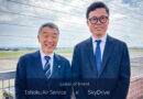 Two men in suits smiling on a rooftop at an airfield, announcing a partnership between Tohoku Air Service and SkyDrive.
