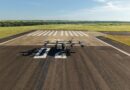default - eVTOL Insights Small propeller aircraft parked on a runway with white striped markings and open fields beyond. (informative)