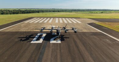 Small propeller aircraft parked on a runway with white striped markings and open fields beyond. (informative)