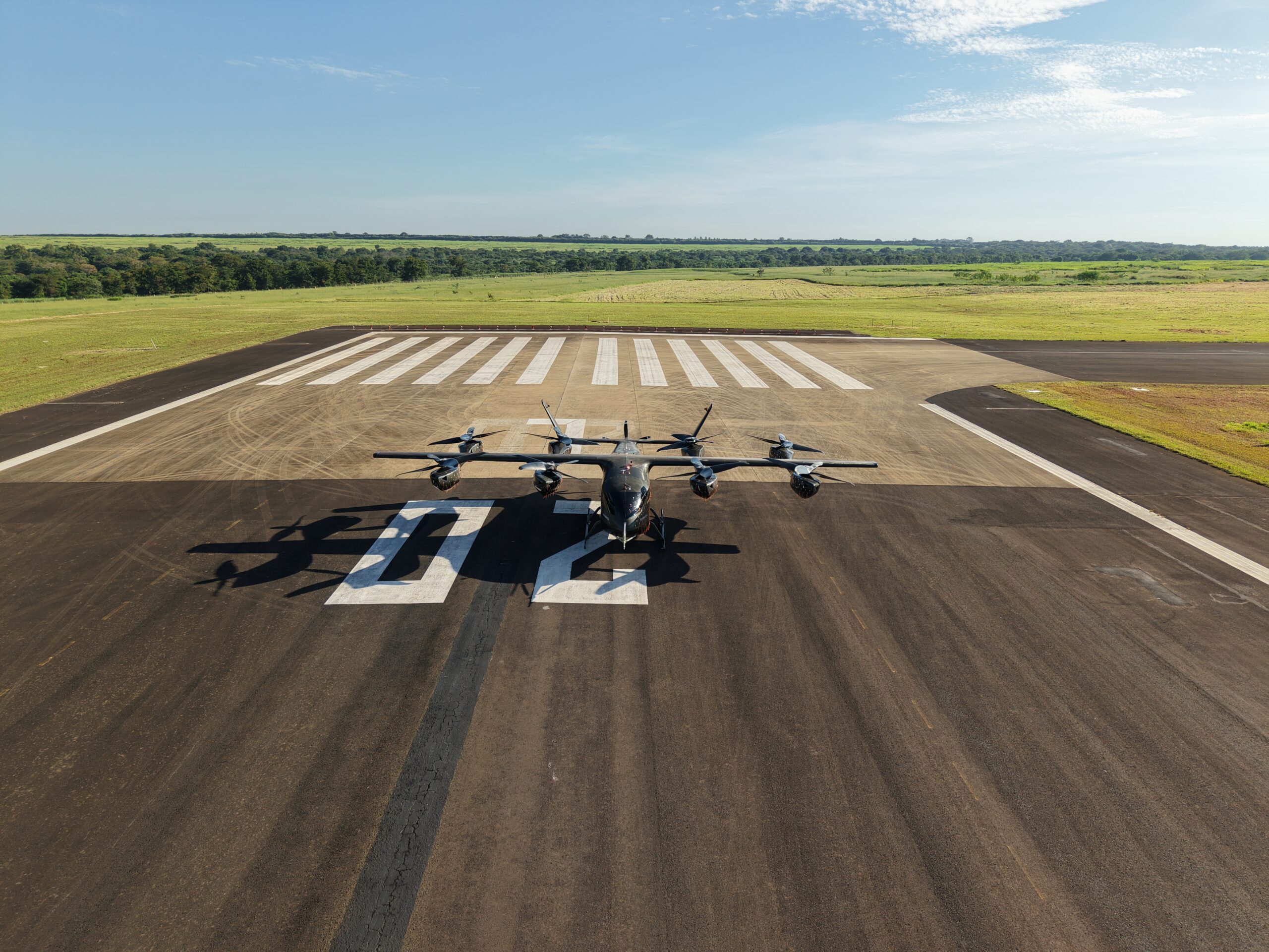 Small propeller aircraft parked on a runway with white striped markings and open fields beyond. (informative)