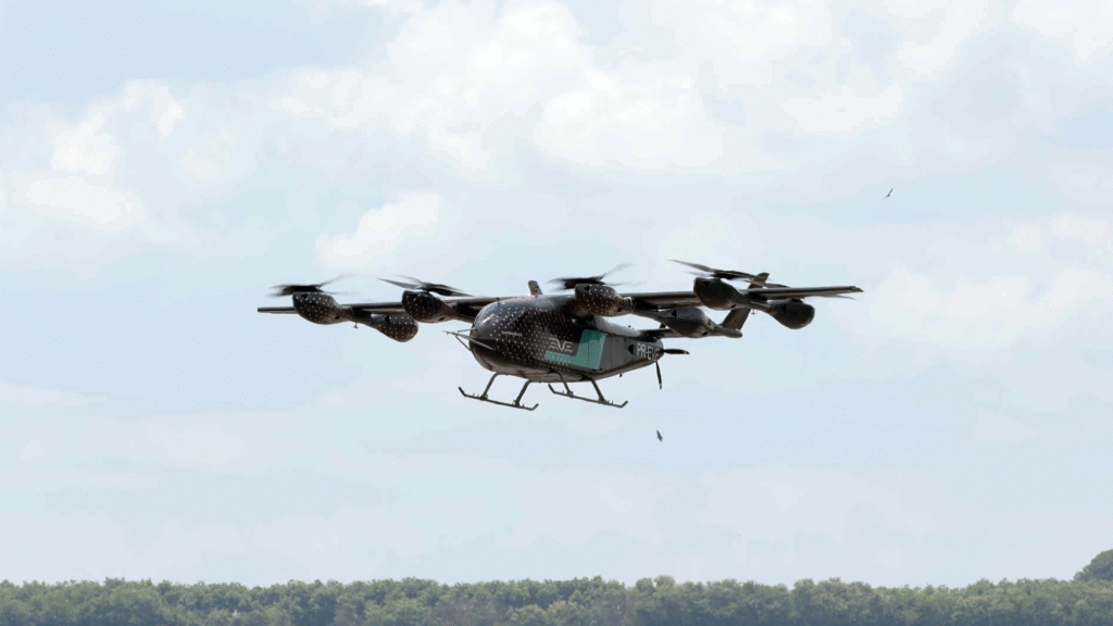 V-22 Osprey tilt-rotor aircraft in flight over a treeline against a cloudy sky, landing gear down.