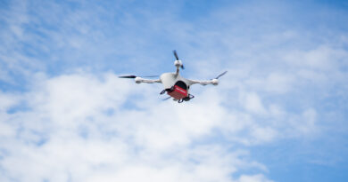 Matternet FINAL image - eVTOL Insights White quadcopter drone with a red cargo box beneath, flying against a blue, partly cloudy sky