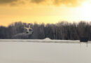 P1035126 2 - eVTOL Insights White helicopter hovering over a snow-covered field with bare trees at sunset