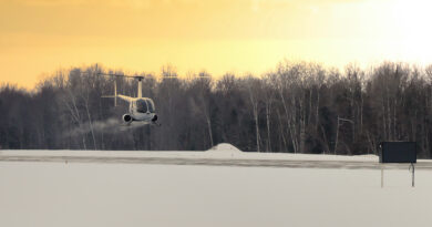 P1035126 2 - eVTOL Insights White helicopter hovering over a snow-covered field with bare trees at sunset