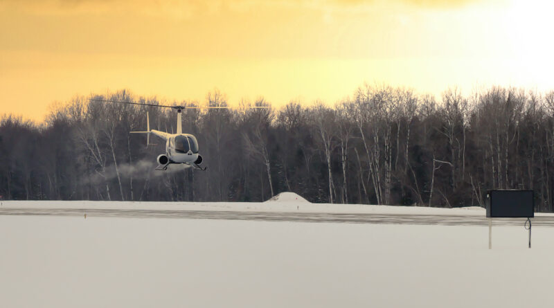 P1035126 2 - eVTOL Insights White helicopter hovering over a snow-covered field with bare trees at sunset