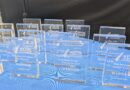 A row of blue glass awards labeled WINNER on a blue table at an awards ceremony display area.