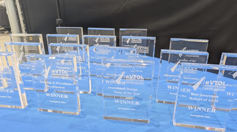 A row of blue glass awards labeled WINNER on a blue table at an awards ceremony display area.