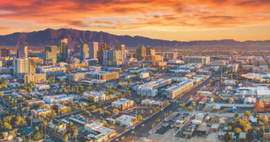 Aerial view of a downtown skyline at sunset with orange-pink clouds and distant mountains on the horizon.