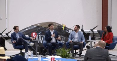 Panel discussion in an aircraft hangar with four speakers seated and a small airplane behind them.
