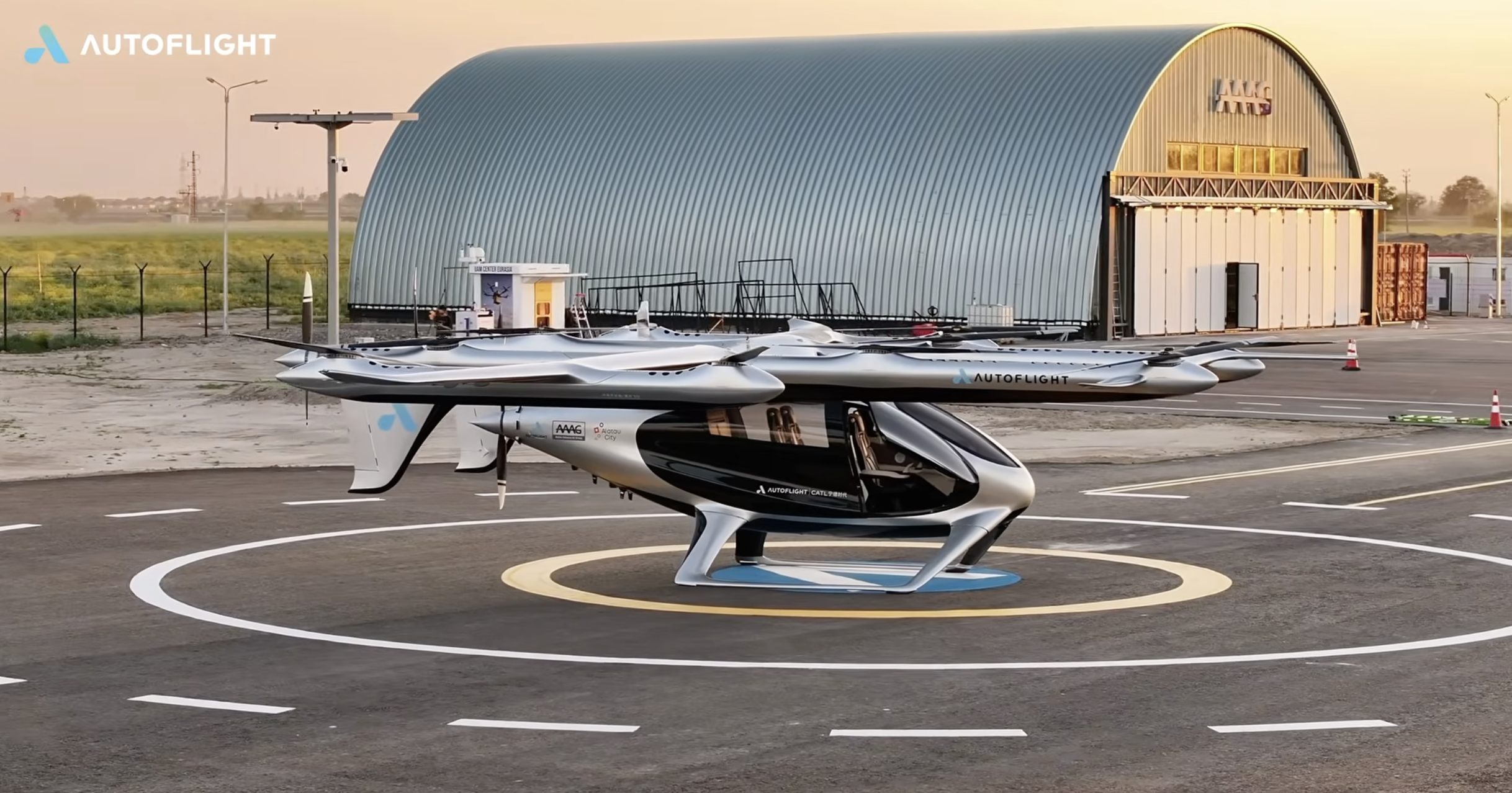 Autoflight logo in the top-left; futuristic aircraft on a circular helipad in front of a curved metal hangar at sunset.