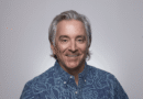 Portrait of a smiling man with gray hair in a blue patterned shirt against a light gray background