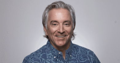 Portrait of a smiling man with gray hair in a blue patterned shirt against a light gray background