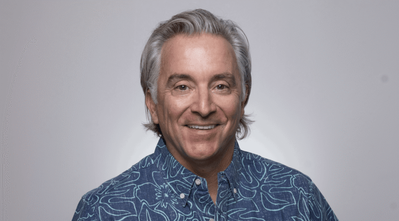 Portrait of a smiling man with gray hair in a blue patterned shirt against a light gray background