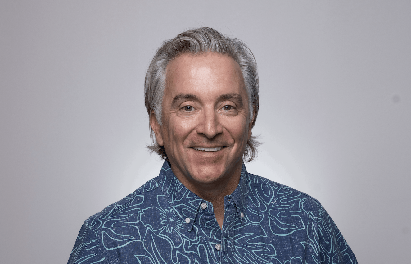 Portrait of a smiling man with gray hair in a blue patterned shirt against a light gray background