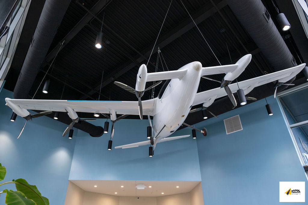 White twin-engine propeller airplane model hanging from the ceiling in a modern blue-walled interior, spotlighting above it