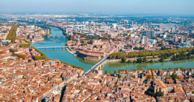 Toulouse aerial panoramic view France - eVTOL Insights Aerial cityscape with a winding river, multiple bridges, and dense red-roofed buildings along green riverbanks.