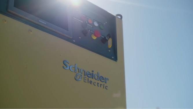Close-up of a yellow Schneider Electric industrial panel with a control screen and colorful buttons, sun glare at top left.