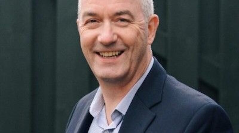 Richard Alexander - eVTOL Insights Smiling man with short gray hair in a blazer and light shirt, outdoors against a dark fence backdrop.