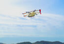 260622_高速飛行_プレスリリース用画像_final_文字無し-2048x1152 - eVTOL Insights Yellow helicopter in midair above a ridge of green hills, against a clear blue sky.