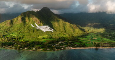 Small white airplane labeled SURFAIR flying over lush green tropical mountains and a coastal shoreline.
