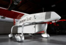 White and red Elroy Air experimental aircraft indoors, shown from the side with visible landing gear and tail section.