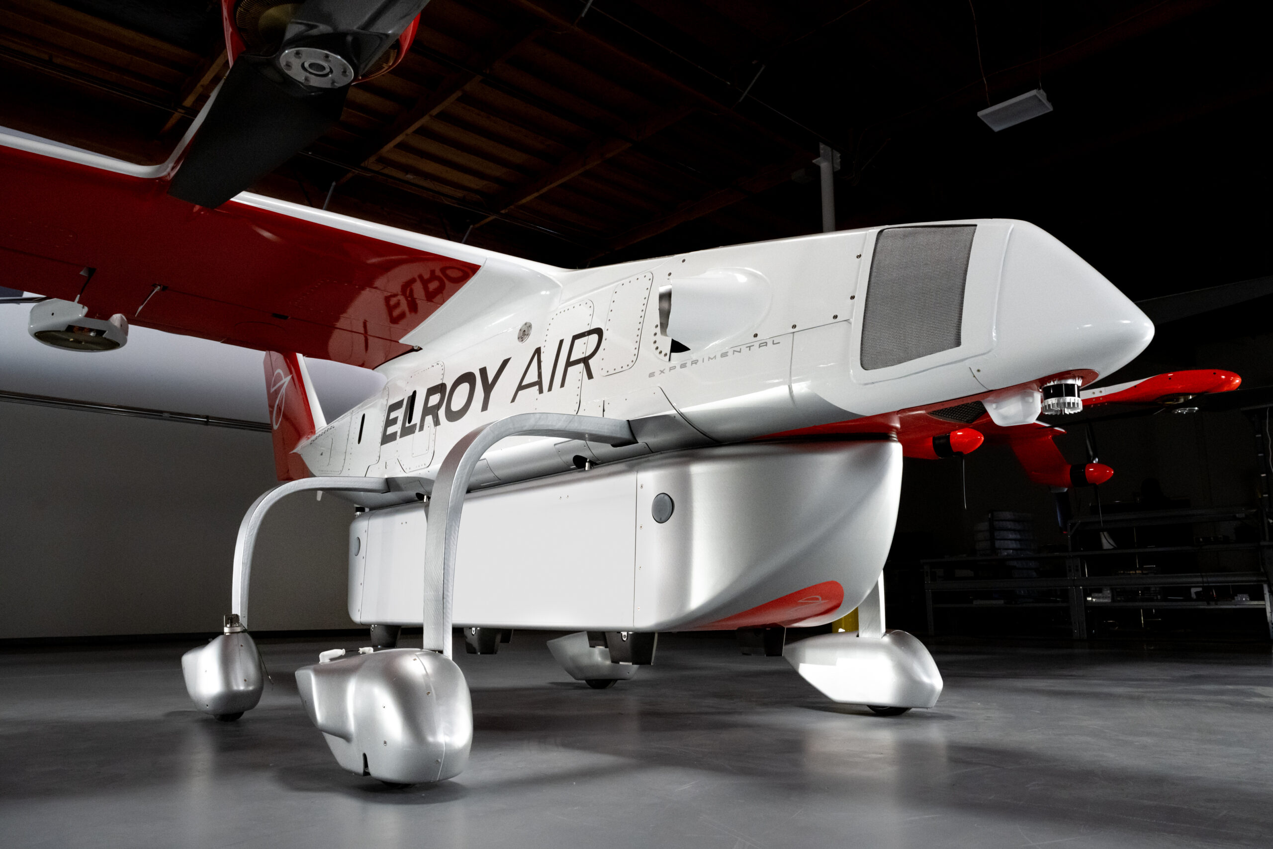 White and red Elroy Air experimental aircraft indoors, shown from the side with visible landing gear and tail section.