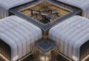 A futuristic rooftop drone hub with a central multi-rotor aircraft on a glass-walled helipad, surrounded by white curved buildings numbered 01–04 at dusk.