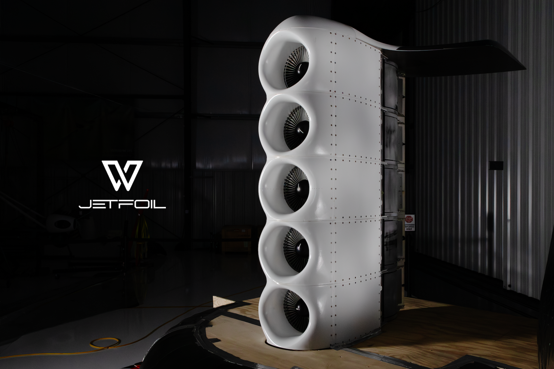 Tall vertical stack of four white turbine fans in a dim hangar, with Jetfoil logo in the lower-left.
