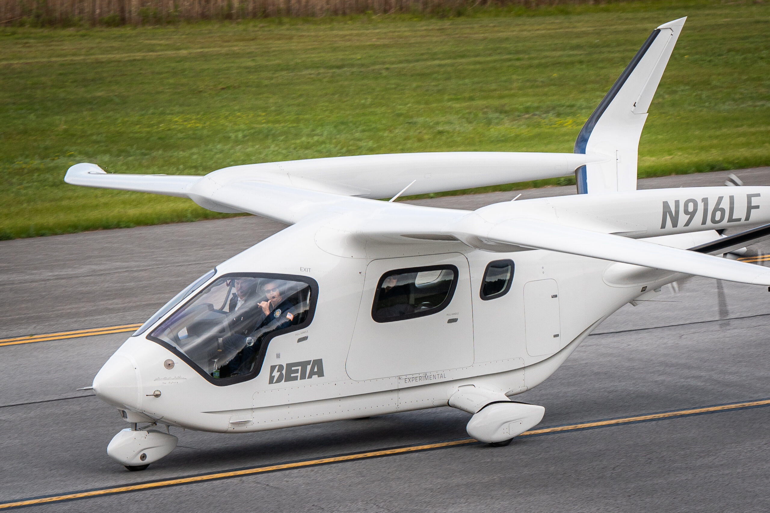 White small aircraft on a runway with two pilots visible in the cockpit and tail number N916LF on the fuselage.