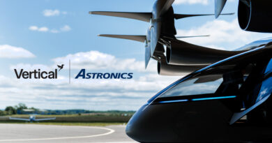 Close-up of a helicopter nose with rotor hub above and the Vertical Astronics logo on the fuselage against a blue sky.