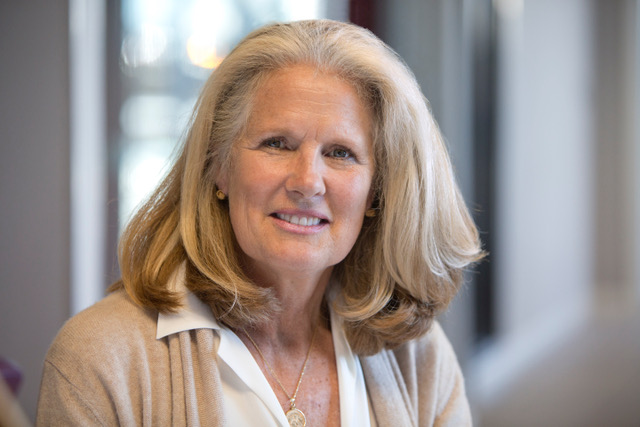 Portrait of a smiling, shoulder-length blonde woman in a white blouse and beige cardigan.