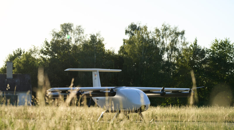 Small white glider aircraft parked on a grassy field with trees in the background and a clear sky above.