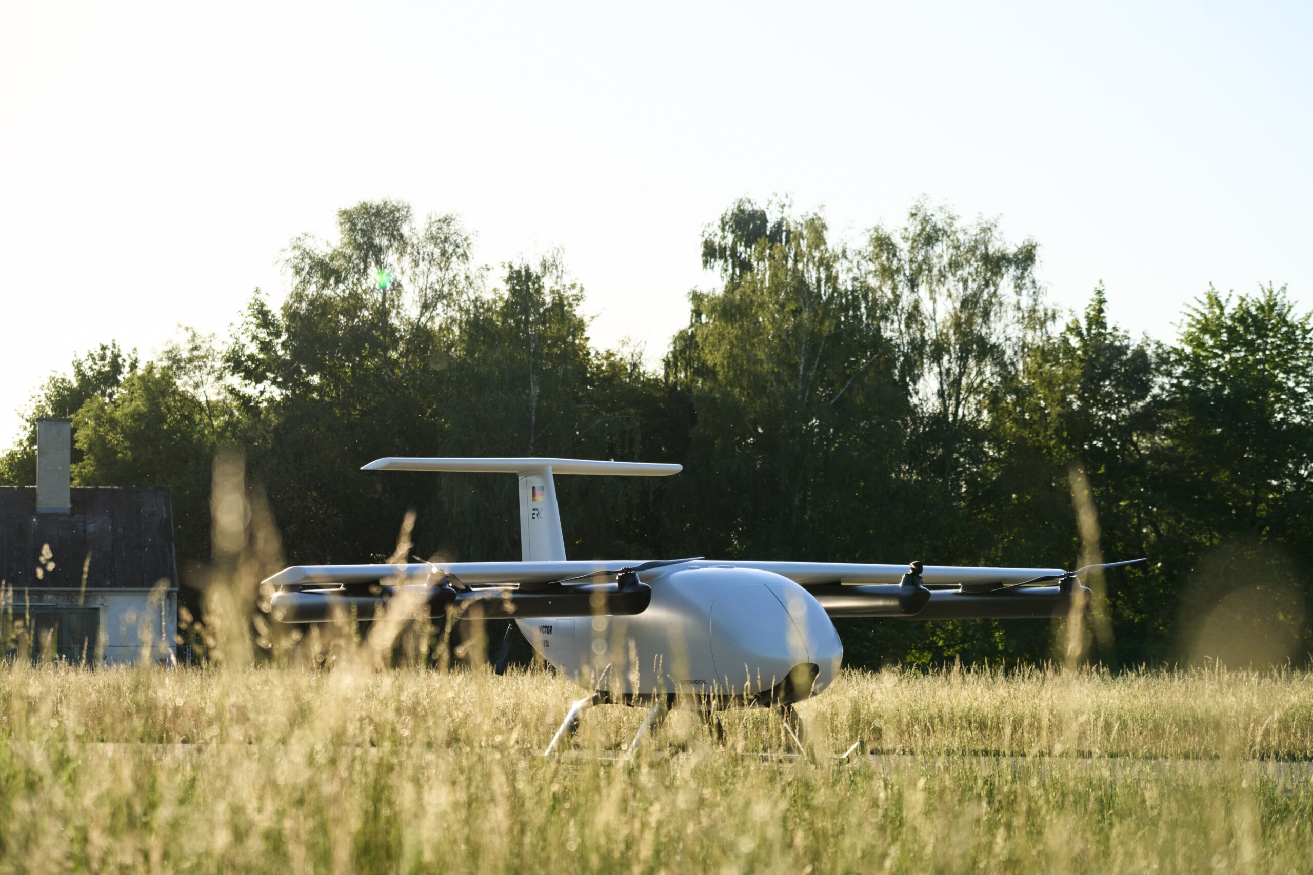 Small white glider aircraft parked on a grassy field with trees in the background and a clear sky above.