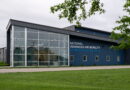 Modern blue building with large glass entrance and a sign reading 'NATIONAL ADVANCED AIR MOBILITY CENTER OF EXCELLENCE'.