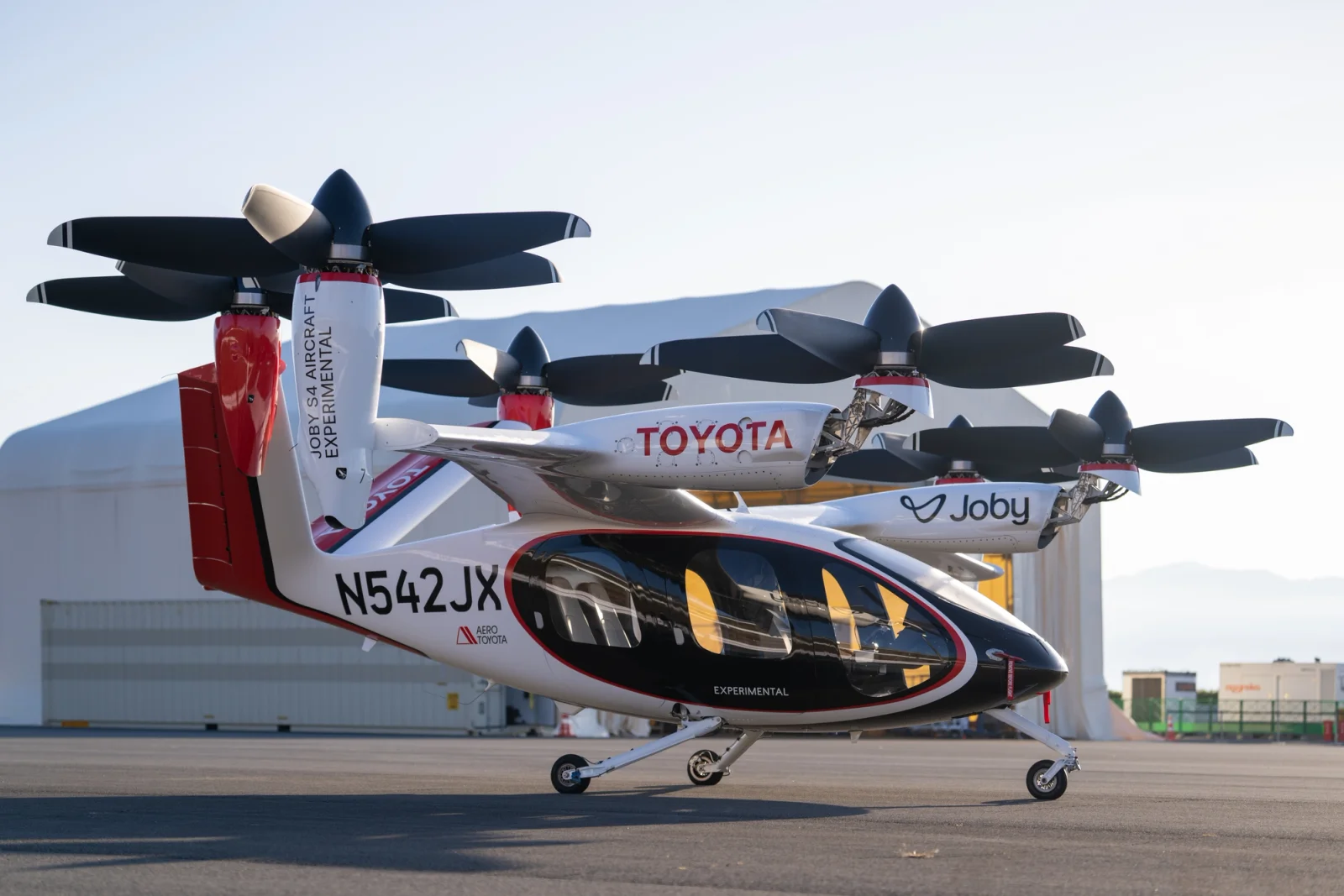Tilt-rotor aircraft on the ground with rotors folded, branded Toyota and Joby, at an airfield.