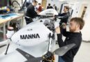 Engineer tightens a component on a white drone-like aircraft labeled MANNÁ in a bright workshop.
