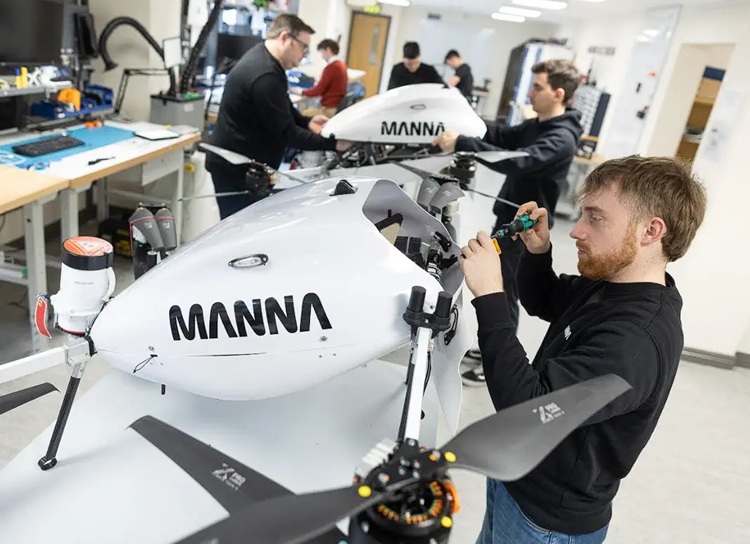 Engineer tightens a component on a white drone-like aircraft labeled MANNÁ in a bright workshop.