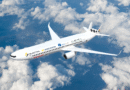White commercial jet soaring above fluffy clouds with branding and logos along the fuselage visible in flight.