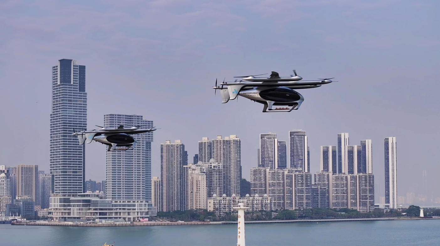 Two futuristic eVTOL aircraft flying over a city skyline by the water at dusk/dawn light.