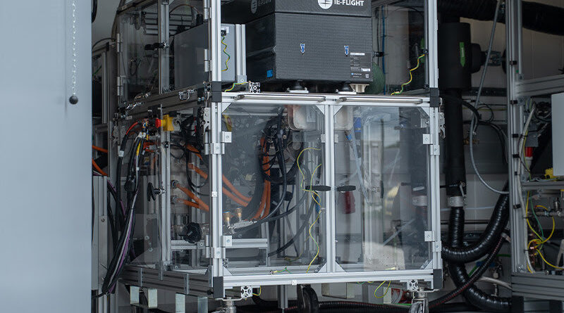 unnamed 53 - eVTOL Insights Wheeled metal-frame equipment cart with a glass enclosure containing electrical components and a tangle of cables in a laboratory.