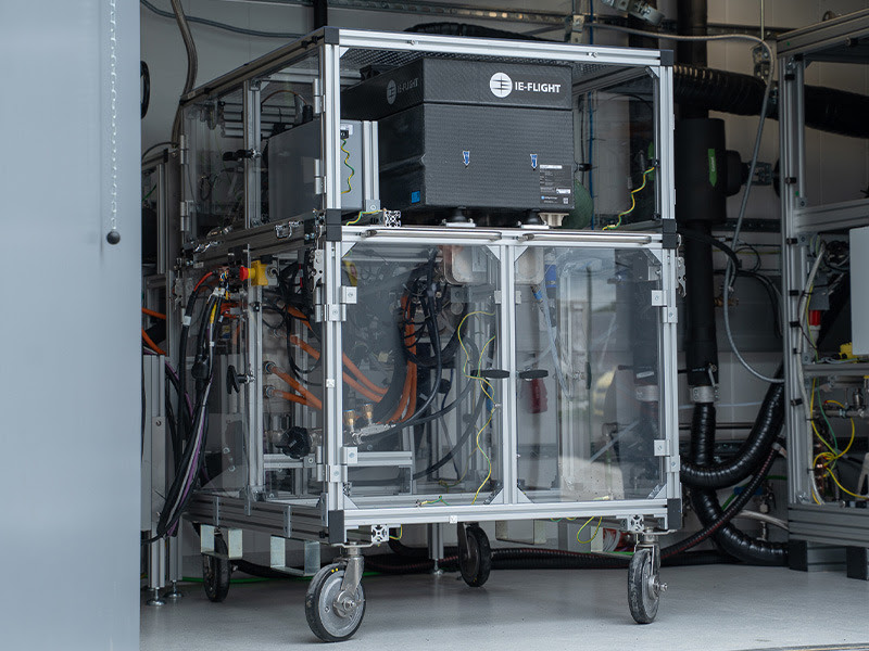 Wheeled metal-frame equipment cart with a glass enclosure containing electrical components and a tangle of cables in a laboratory.